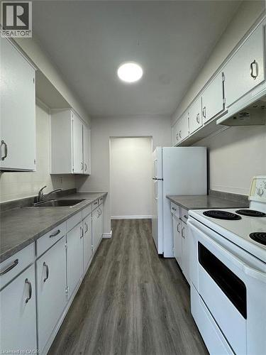 Galley kitchen featuring white cabinetry, dark gray countertops, stainless steel sink, and wood-finish flooring - 232 Louisa Street Unit# 9A, Kitchener, ON - Indoor Photo Showing Kitchen