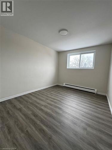 Light-filled room featuring wood-finish flooring, neutral wall tones, a modern ceiling light fixture, and a white-framed window - 232 Louisa Street Unit# 9A, Kitchener, ON - Indoor Photo Showing Other Room