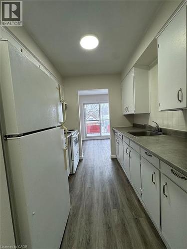 Galley kitchen with wood-finish flooring, white cabinetry, dark countertops, and a full suite of white appliances - 232 Louisa Street Unit# 9A, Kitchener, ON - Indoor Photo Showing Kitchen