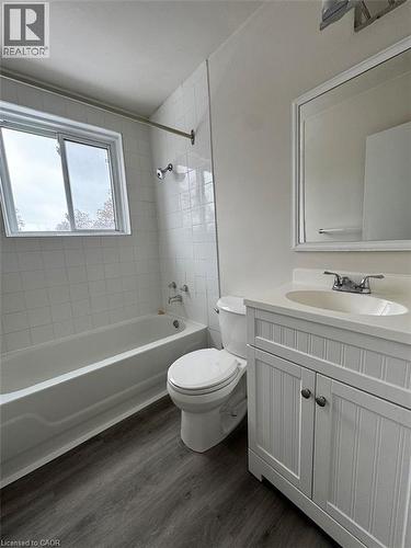 Full bathroom featuring a white tile tub surround, white vanity with beadboard paneling, and wood-finish flooring - 232 Louisa Street Unit# 9A, Kitchener, ON - Indoor Photo Showing Bathroom
