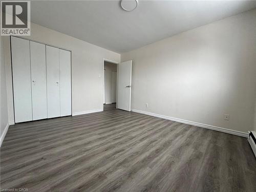Spacious room featuring wood-finish flooring, light neutral wall tones, white baseboards, and a ceiling light fixture - 232 Louisa Street Unit# 9A, Kitchener, ON - Indoor Photo Showing Other Room