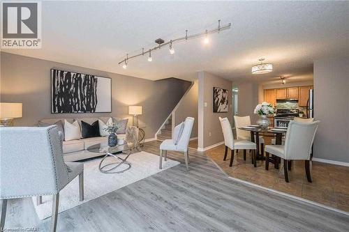 Open-concept living and dining areas featuring wood-finish flooring, track lighting, a staircase with carpeting, and an adjacent kitchen with wood cabinetry - 27 Max Becker Drive, Kitchener, ON - Indoor