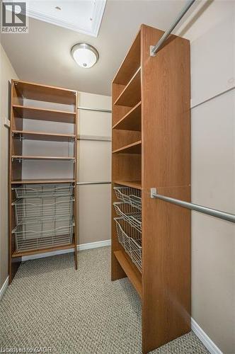 Walk-in closet featuring built-in wood-finish shelving, metal hanging rods, integrated wire baskets, and patterned carpet flooring - 27 Max Becker Drive, Kitchener, ON - Indoor