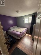 Bedroom featuring wood-finish flooring and a single window with dark window treatments - 