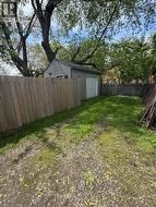 Detached garage with horizontal siding and a single overhead door, situated within a fenced rear yard featuring a wood privacy fence and mature trees - 