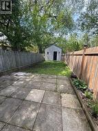 Expansive outdoor space featuring a paved patio, a detached storage shed with a window and single door, a wooden fence, and mature trees providing natural canopy - 