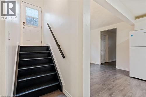 Entryway featuring a white door with frosted glass paneling, a dark-toned staircase with a black handrail, and wood-finish flooring extending into the adjacent space - 9 Cherry Street, Simcoe, ON - Indoor Photo Showing Other Room