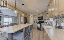 Kitchen featuring a large eat-at island, pendant lighting, herringbone tile backsplash, wood-finish flooring, and black appliances - 