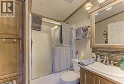 3 piece Bathroom featuring a shower with a sliding glass door, a vanity with a white countertop and sink, a medicine cabinet with integrated lighting, a tile backsplash, and built-in cabinetry - 