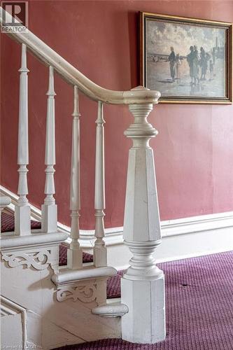 Ornate white wooden newel post and balusters with carved detailing, framing a staircase featuring purple patterned carpeting - 370 Hess Street S, Hamilton, ON - Indoor