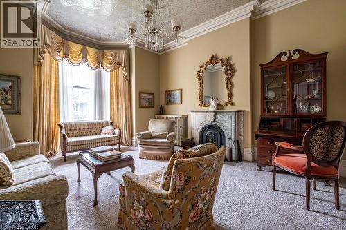 Spacious room featuring a grand bay window with custom drapery, an ornate ceiling medallion, a decorative fireplace with a substantial mantel, and crown molding - 370 Hess Street S, Hamilton, ON - Indoor Photo Showing Living Room With Fireplace