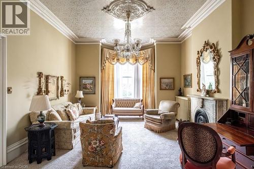 Living area featuring an ornate ceiling medallion, crystal chandelier, decorative ceiling, bay window, and a marble fireplace with a decorative mantel and hearth - 370 Hess Street S, Hamilton, ON - Indoor