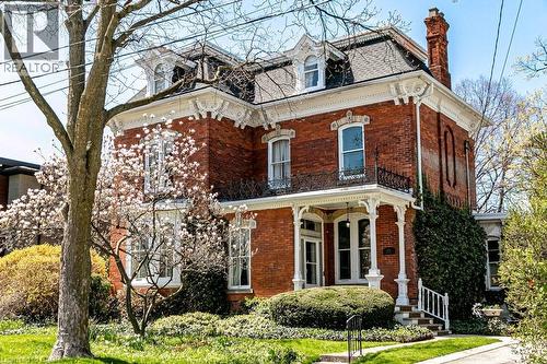 Brick exterior featuring an intricate white cornice, multiple dormer windows, a covered front porch with decorative columns, and an ornate second-story balcony - 370 Hess Street S, Hamilton, ON - Outdoor