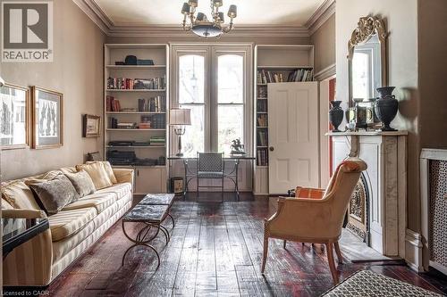 Living area featuring wood-finish flooring, built-in shelving, a decorative fireplace with a mantel, double windows, and a chandelier - 370 Hess Street S, Hamilton, ON - Indoor Photo Showing Living Room