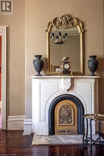 Marble fireplace surround with a decorative brass firebox cover, featuring an ornate gold-framed mirror above - 370 Hess Street S, Hamilton, ON - Indoor