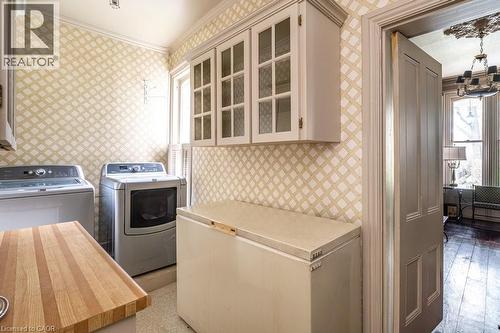 Dedicated utility space featuring light-toned cabinetry with glass inserts, a butcher block countertop, and patterned wall covering - 370 Hess Street S, Hamilton, ON - Indoor Photo Showing Laundry Room