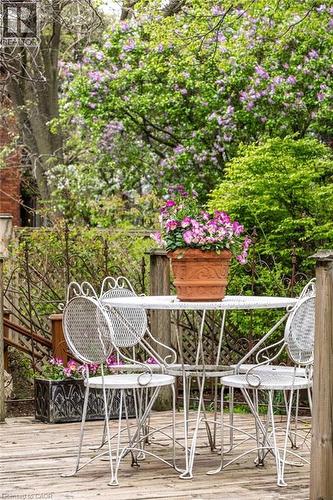 Outdoor deck space featuring natural wood planks, a classic wrought iron patio set, and vibrant background foliage - 370 Hess Street S, Hamilton, ON - Outdoor