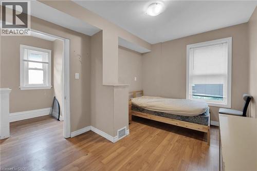 Neutral-toned room featuring wood-finish flooring and a white-framed window with blinds - 738 King Street W, Hamilton, ON - Indoor Photo Showing Bedroom