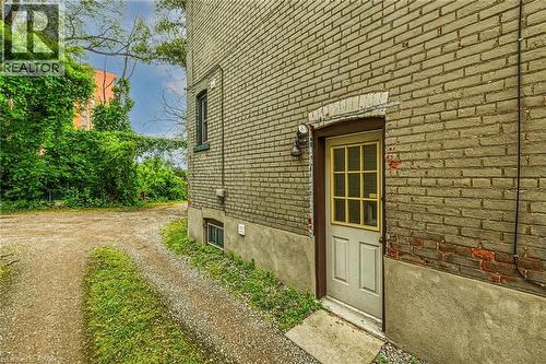 Brick exterior featuring a basement entry door with windowpanes and an exterior light fixture - 738 King Street W, Hamilton, ON - Outdoor