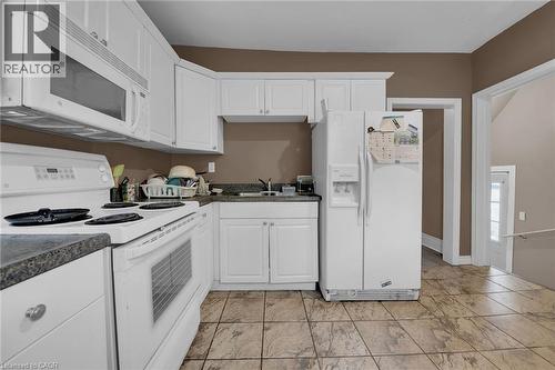 Kitchen featuring white cabinetry, dark speckled countertops, and integrated appliances - 738 King Street W, Hamilton, ON - Indoor Photo Showing Kitchen With Double Sink