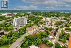 Aerial perspective showcasing the surrounding urban landscape with extensive tree canopy, multi-lane roadways, and various architectural styles including high-rise residential buildings and lower-rise - 