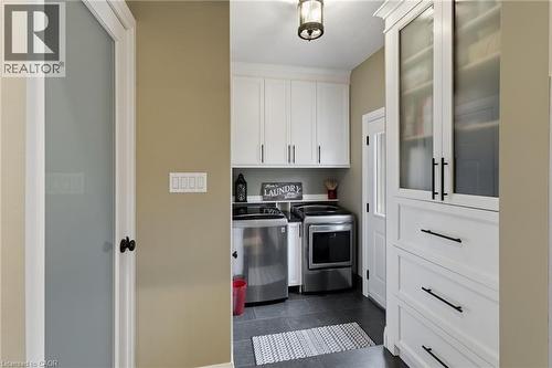 Dedicated laundry area featuring white cabinetry, dark hardware, stainless steel appliances, dark tile flooring, and a frosted glass door - 2116 Binbrook Road E, Hamilton, ON - Indoor