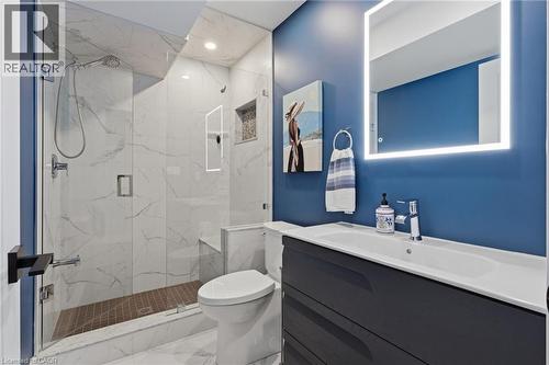 Bathroom featuring a glass-enclosed shower with a built-in bench, marble-finish wall and floor tile, a dark blue vanity, and an illuminated mirror - 2116 Binbrook Road E, Hamilton, ON - Indoor Photo Showing Bathroom
