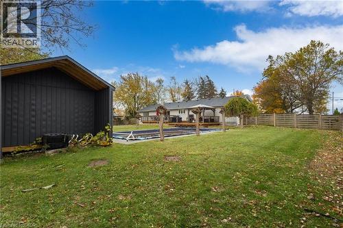 Expansive backyard featuring a covered pool, detached storage shed with dark vertical siding, a wooden privacy fence, and mature trees - 2116 Binbrook Road E, Hamilton, ON - Outdoor With Deck Patio Veranda