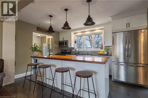 Kitchen featuring a central island with a wood-finish countertop, white cabinetry, stainless steel appliances, a tile backsplash, and dark tile flooring - 2116 Binbrook Road E, Hamilton, ON - Indoor Photo Showing Kitchen