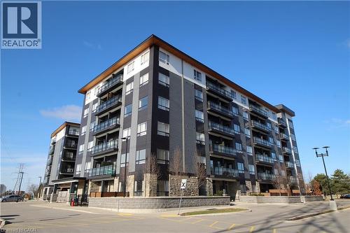 Contemporary multi-story building featuring black, white, and grey siding, private balconies with glass railings, and a wood-finish soffit - 247 Northfield Drive E Unit# 207, Waterloo, ON - Outdoor With Balcony With Facade
