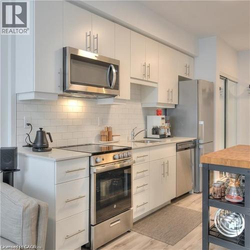 Contemporary kitchen featuring white cabinetry, stainless steel appliances, light-toned countertops, subway tile backsplash, Pictured island not included. An island will be in place for new tenant. - 247 Northfield Drive E Unit# 207, Waterloo, ON - Indoor Photo Showing Kitchen With Stainless Steel Kitchen With Upgraded Kitchen