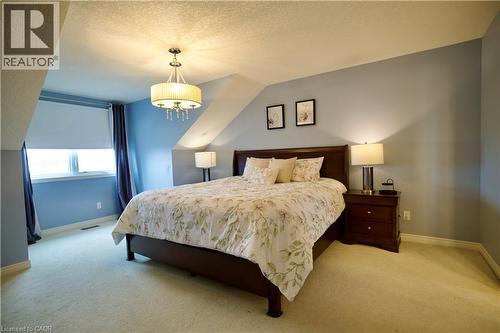 Carpeted room featuring a window with roller shade, sloped ceilings, and a decorative ceiling light fixture - 704 Zurich Drive, Waterloo, ON - Indoor Photo Showing Bedroom