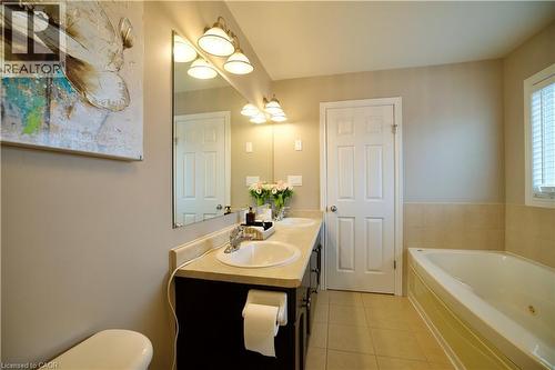Bathroom featuring a dual-sink vanity with light-toned countertop, a large wall mirror, and a built-in tub with tile surround - 704 Zurich Drive, Waterloo, ON - Indoor Photo Showing Bathroom