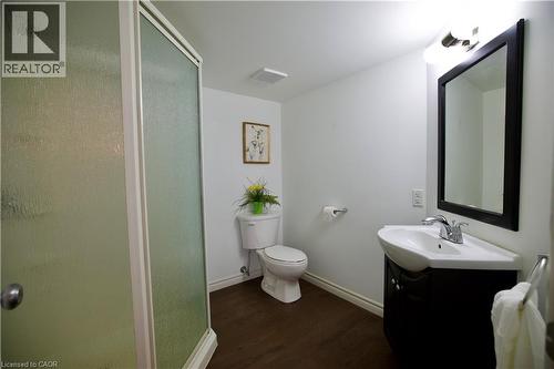 Full bathroom featuring a walk-in shower with textured glass, a modern vanity with integrated sink, a large framed mirror, and wood-finish flooring - 704 Zurich Drive, Waterloo, ON - Indoor Photo Showing Bathroom