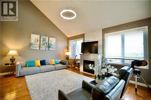 Vaulted ceiling living room featuring wood-finish flooring, a contemporary fireplace with a white mantel, and large windows with blinds - 704 Zurich Drive, Waterloo, ON - Indoor Photo Showing Living Room With Fireplace