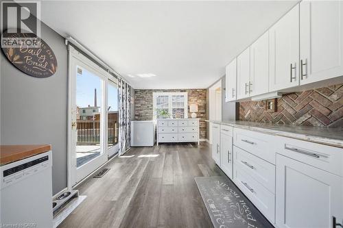 Modern kitchen featuring white shaker cabinetry with brushed nickel hardware, a brick-patterned backsplash, and wood-finish flooring - 401 West Street, Simcoe, ON - Indoor Photo Showing Kitchen