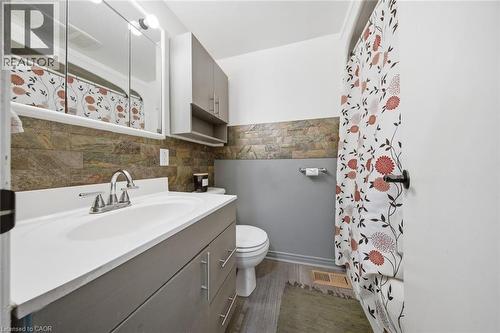 Bathroom featuring a single vanity with a white countertop and chrome faucet, stacked upper cabinetry, natural stone tile wainscoting, and wood-finish flooring - 401 West Street, Simcoe, ON - Indoor Photo Showing Bathroom