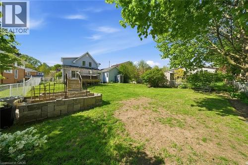 Spacious backyard featuring a large lawn area, a multi-tiered stone retaining wall, and a wooden deck with stairs - 401 West Street, Simcoe, ON - Outdoor