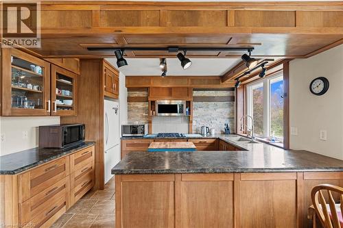 Kitchen featuring a U-shaped countertop layout with dark stone-finish surfaces, extensive wood cabinetry, and a stone tile backsplash - 3 San Pedro Drive, Hamilton, ON - Indoor Photo Showing Kitchen