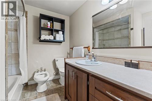 Bathroom featuring a combination bathtub and shower with tile surround, a built-in wood-finish vanity with an integrated sink, a large wall-mounted mirror, and tile flooring - 3 San Pedro Drive, Hamilton, ON - Indoor Photo Showing Bathroom