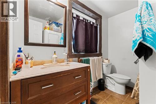 Bathroom featuring a wood-finish vanity with an integrated sink and light-toned countertop, framed mirror, and a window with dark trim - 3 San Pedro Drive, Hamilton, ON - Indoor Photo Showing Bathroom