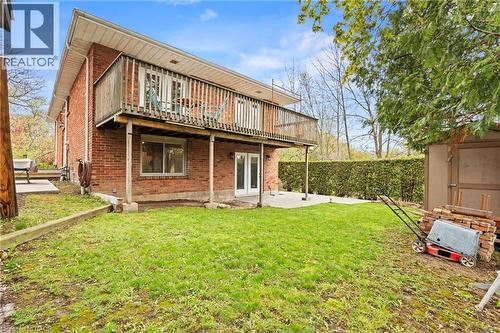 Brick exterior with a second-story wooden deck, ground-level patio, and a spacious green lawn - 3 San Pedro Drive, Hamilton, ON - Outdoor With Deck Patio Veranda