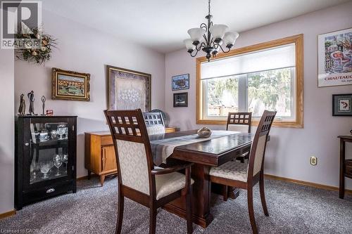 Dining area featuring an overhead chandelier with five frosted glass shades, a large window with natural wood trim, and textured gray carpeting - 19 Chateau Court, Hamilton, ON - Indoor Photo Showing Dining Room