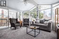 Sunroom featuring an angular wall of windows, a vaulted ceiling with a ceiling fan, plush gray carpeting, and a sliding glass door providing exterior access - 