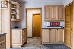 Light wood-finish cabinetry featuring curved open shelving, stone-finish countertops, and under-cabinet lighting - 