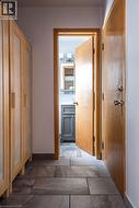 Hallway featuring large format rectangular tile flooring, natural wood-finish doors, and built-in cabinetry with frosted glass panels - 