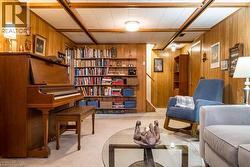 Finished basement space featuring extensive wood paneling, exposed ceiling beams, built-in shelving, carpeted flooring, and a glass-top coffee table - 