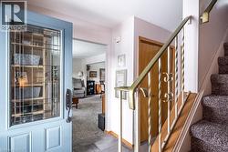 Entryway featuring a blue paneled door with decorative glass, tiled flooring, and a carpeted staircase with a brass-toned metal railing - 