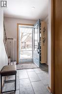 Entryway featuring large format rectangular floor tiles, a light blue main door with glass panels, a recessed ceiling light, and a built-in light wood storage unit - 