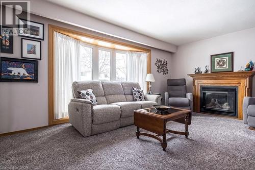 Living area featuring a prominent wood fireplace with a detailed mantel, a bay window with a wood-finish frame, light-toned wall paint, and gray carpet flooring - 19 Chateau Court, Hamilton, ON - Indoor Photo Showing Living Room With Fireplace